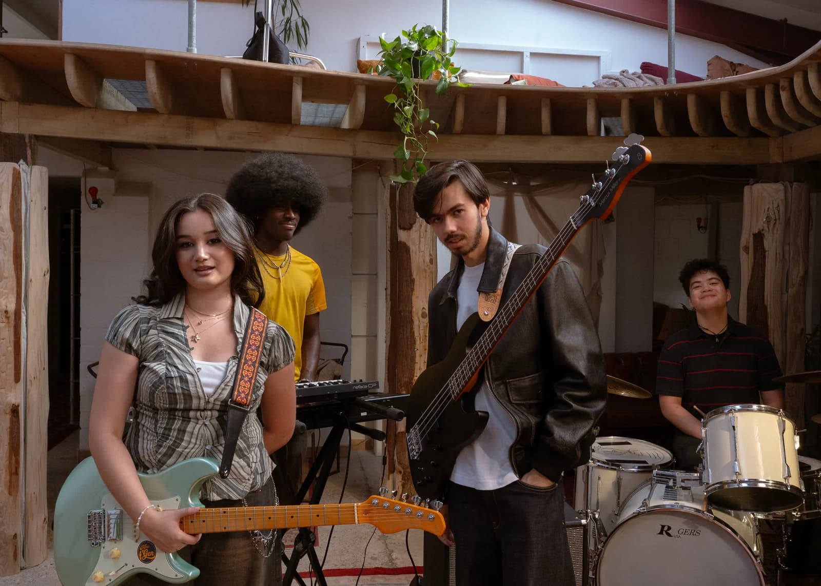 Clarissa Mae holding a seafoam-green Sire guitar with the band on the bed crumbs music video set