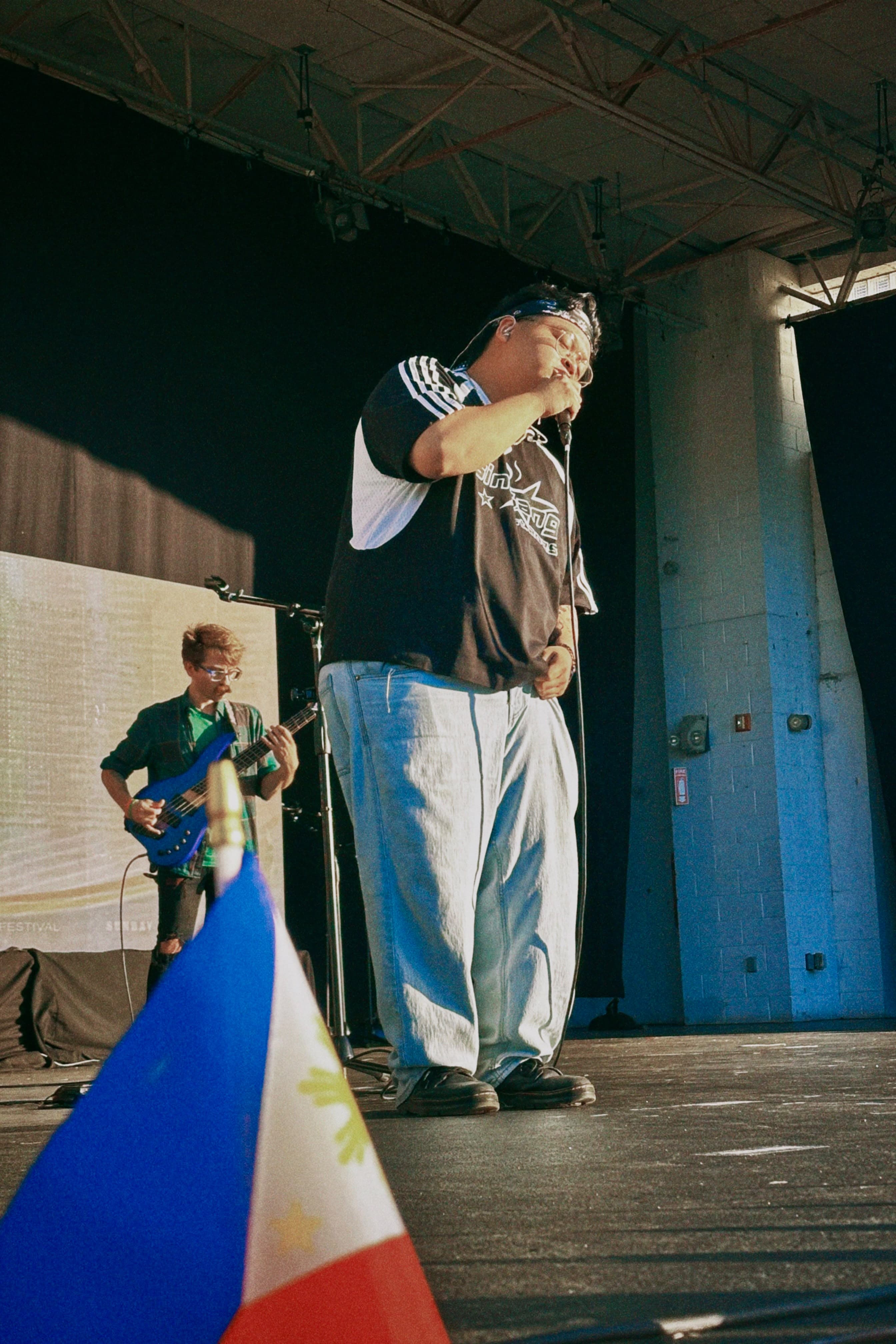 Justin Magnaye singing beside a Philippine flag during his Filipino American Festival set